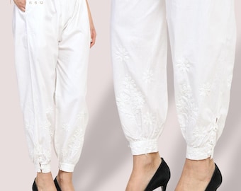 Può includere: Pantaloni bianchi ricamati con vita con coulisse e caviglie elasticizzate. I pantaloni presentano ricami floreali intorno alle caviglie e un dettaglio con bottoni sul lato. Il nome del marchio "hirfat" è visibile in alto a sinistra.
