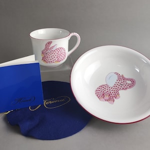May include: A pink and white porcelain teacup and saucer set featuring a pink rabbit and elephant design. The set is part of a children's tea set.