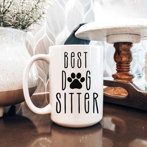May include: White ceramic coffee mug with a black paw print and the text "Best Dog Sitter" in black.