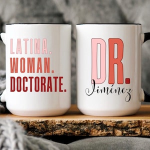 May include: Two white ceramic mugs with black handles and rims. One mug displays the text "LATINA. WOMAN. DOCTORATE." in gradient pink and red. The other mug has "DR." in pink and red, with the name "Jiménez" in cursive.