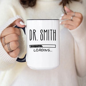 May include: White ceramic mug with a black rim and handle. The mug has black text that reads "DR. SMITH" and a black progress bar with the text "LOADING..." below it.
