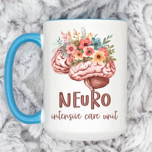 May include: White ceramic mug with a blue handle and rim. The mug features a brain illustration adorned with colorful flowers. The words "NEURO intensive care unit" are printed in brown.