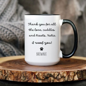 May include: White ceramic mug with a black rim and handle. The mug has a paw print and the text "Thank you for all the love, cuddles and treats, Katie. I woof you! BROWNIE" printed on it.
