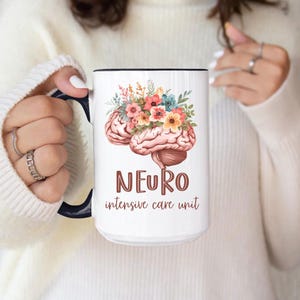 May include: White ceramic mug with a black interior and handle. The mug features a watercolor illustration of a brain with colorful flowers and the text "NEURO intensive care unit" in brown.