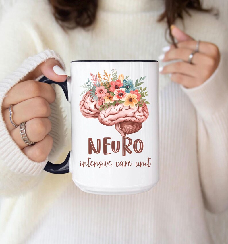 May include: White ceramic mug with a black interior and handle. The mug features a watercolor illustration of a brain with colorful flowers and the text "NEURO intensive care unit" in brown.