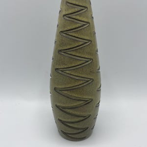 May include: A tall, green ceramic vase with a textured, geometric pattern. The vase has a narrow opening and a rounded base.