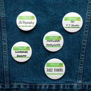 Op de afbeelding: Vijf witte buttons met groene en gele accenten. Elke button heeft het woord "HELLO" en een naam of zin, waaronder "Sh'Dynasty", "Gus", "Lavender Gooms", "Methuselah Honeysuckle" en "Jazz Hands".