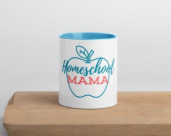 Puede incluir: Taza de cerámica blanca con borde azul. La taza presenta un contorno azul de una manzana con una hoja verde y el texto "Homeschool MAMA" en azul y rojo.