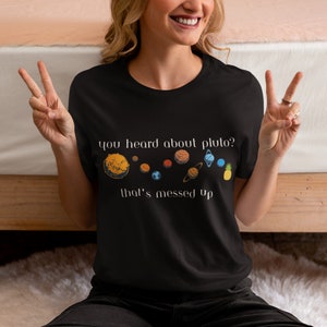 Puede incluir: Una camiseta negra con un estampado gráfico blanco de un sistema solar con el texto "you heard about pluto? that's messed up".