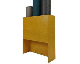 May include: A mustard yellow wooden storage unit with a rectangular design. It features an open shelf at the bottom and holds four rolled-up yoga mats in shades of gray and teal. The mats are of varying sizes and textures.