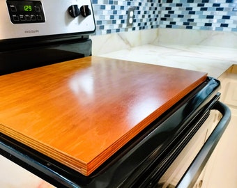 May include: A close-up of a black stovetop with a wooden cutting board on top. The stovetop has a digital display that reads "12:9".
