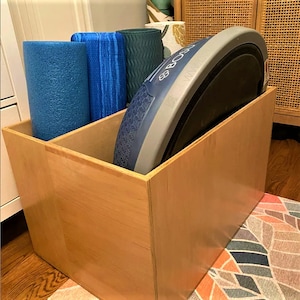 May include: A wooden storage box with a blue and gray BOSU ball and three blue yoga mats inside.