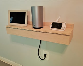 May include: A light wood shelf mounted on a wall with a white digital picture frame, a silver cylindrical device, and a white baby monitor with an antenna.