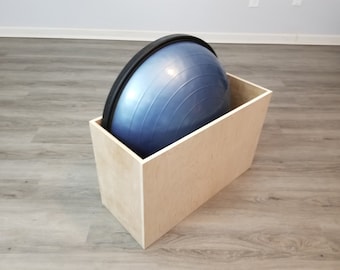 May include: A light wood storage box with a blue and black exercise ball inside.