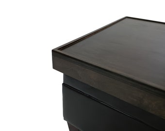 May include: Close-up of the top of a dark brown wooden storage ottoman with a black leather upholstered base.