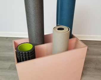 May include: A pink storage box with three rolled up exercise mats. The mats are gray, blue, and beige. A black foam roller with a green center is also in the box.