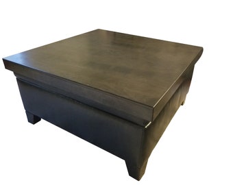 May include: A dark brown wooden coffee table with a black leather top and four legs. The table has a storage compartment.