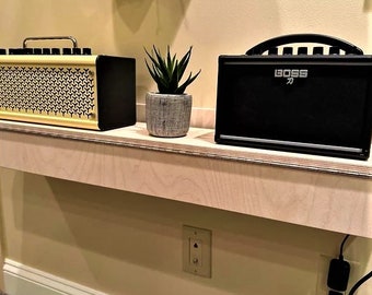 May include: Two small guitar amplifiers on a wooden shelf. The amplifier on the left is yellow with a black speaker grill. The amplifier on the right is black with the word "BOSS" printed on it. A small potted plant sits on the shelf between the amplifiers.