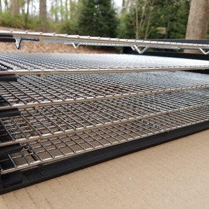May include: A black food dehydrator with five chrome-plated wire mesh trays. The trays are stacked inside the dehydrator, which is made of black plastic.