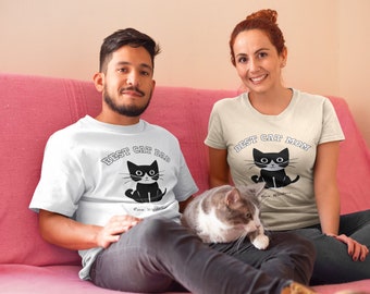 May include: Two people wearing white t-shirts with a black cat graphic and text. One shirt says "Best Cat Dad" and the other says "Best Cat Mom". A gray and white cat sits on the lap of the person wearing the "Best Cat Dad" shirt.