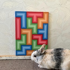 May include: A colorful abstract painting with a geometric design in shades of red, blue, green, and orange. A small rabbit with black and white fur is in the foreground. The painting is on a rectangular canvas.