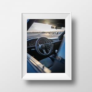 May include: A close-up view of the interior of a car, showing the steering wheel, dashboard, and seats. The steering wheel is black with a silver Mercedes-Benz logo and a yellow stripe. The dashboard is black with silver accents. The seats are black with a chequered pattern.