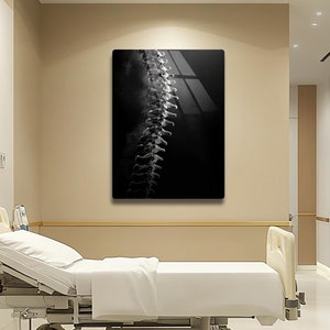 Può includere: Un letto d'ospedale bianco con un lenzuolo bianco e una fotografia in bianco e nero di una colonna vertebrale appesa al muro dietro.