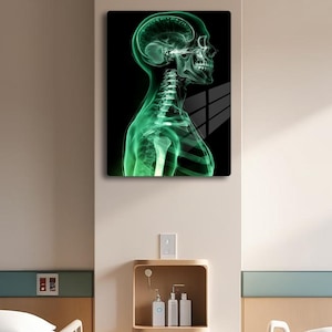 May include: A green and black image of a human skeleton, with the skull and spine visible, is displayed on a wall in a hospital room. Two hospital beds with white linens are in the room, and a small cabinet with drawers and bottles is in the center of the room.