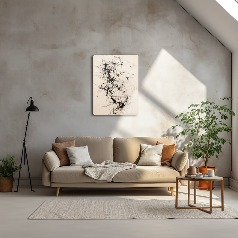 Puede incluir: Un sof&aacute; beige con una manta blanca y almohadas se encuentra en una habitaci&oacute;n con una pared de concreto. Una pintura abstracta en blanco y negro cuelga de la pared sobre el sof&aacute;. Una peque&ntilde;a mesa redonda con una planta en maceta y un libro se encuentra junto al sof&aacute;.