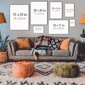 Puede incluir: Una maqueta de dise&ntilde;o de interiores de sala de estar que muestra diferentes tama&ntilde;os de obras de arte enmarcadas en una pared gris. Las obras de arte se muestran sobre un sof&aacute; gris con almohadas de tiro con patrones naranja y negro. El sof&aacute; est&aacute; frente a una alfombra blanca con un patr&oacute;n geom&eacute;trico blanco y negro. Hay dos pufs frente al sof&aacute;, uno naranja y uno verde. La habitaci&oacute;n est&aacute; decorada con una planta en maceta y dos l&aacute;mparas.
