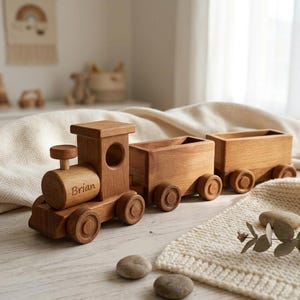 May include: A wooden toy train set with three cars. The engine has a circular smokestack and the name "Brian" engraved on the side. The train is made of light brown wood and has circular wheels.