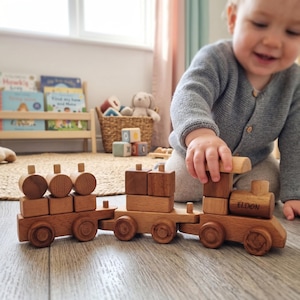 Könnte beinhalten: Ein Holzspielzeugzug mit drei Waggons. Der Zug ist aus hellbraunem Holz gefertigt und hat abgerundete Räder. Auf dem vorderen Waggon steht der Name "ELDON". Der Zug steht auf einem Holzboden.