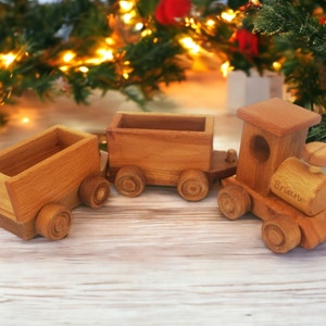 May include: A wooden toy train with three cars, including an engine and two cargo cars. The train is made of light brown wood and has wheels. The engine has the name "Brian" engraved on it. The background includes Christmas decorations.