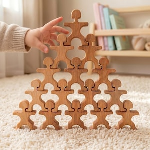 Könnte beinhalten: Ein Holz-Stapelspielzeug in Form von Menschen, angeordnet in einer Pyramide. Die Figuren in Naturholzoptik sind ineinander verschlungen und bilden eine ausgewogene Struktur. Das Spielzeug liegt auf einem weißen Teppich.