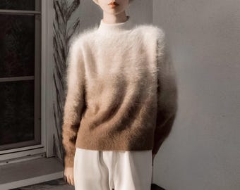 Puede incluir: Un suéter difuso de estilo ombre en tonos de blanco, beige y marrón. El suéter tiene un cuello alto y mangas largas. El modelo lleva pantalones blancos. El suéter parece suave y cómodo.
