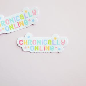 May include: Two stickers with the words "Chronically Online" in pastel colors. The stickers have a white border and are decorated with stars. The background is a solid light pink.