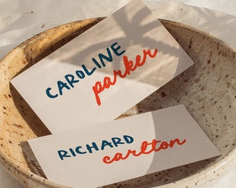 May include: Two white cards with blue and red handwritten names in a speckled brown bowl. The names on the cards are "CAROLINE parker" and "RICHARD carlton".