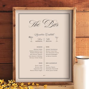 May include: A framed bar menu sign with a light beige background and black text. The header reads The Bar, followed by Signature Cocktails, Hers Margarita, His Martini, and lists of spirits, wines, beer, and non-alcoholic drinks in a clean font.