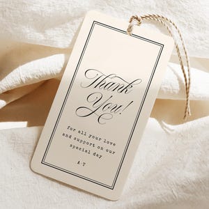 Peut inclure: Une étiquette rectangulaire en papier blanc cassé avec des coins arrondis et une fine bordure noire. Le texte indique Thank You! for all your love and support on our special day A T. Une fine ficelle beige est passée dans un trou en haut.