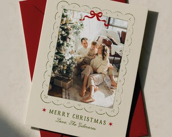 Könnte beinhalten: Eine cremefarbene Weihnachtsgrußkarte mit gewelltem Rand und einer roten Schleifenillustration oben. In der Mitte befindet sich ein Foto einer Familie neben einem Weihnachtsbaum. Der Text lautet: MERRY CHRISTMAS, Love, The Gilmores.