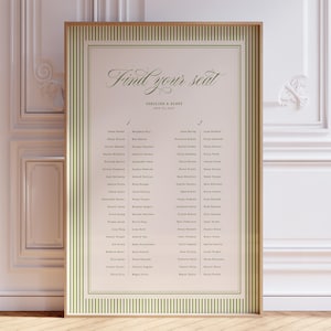 Puede incluir: Un cartel rectangular de distribución de asientos para bodas en un marco de madera clara. El cartel tiene un fondo crema con un borde de rayas verticales verdes. Muestra el texto Find your seat, Caroline & Aaron y una lista de nombres.