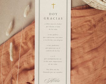 Könnte beinhalten: Eine cremefarbene rechteckige Karte mit einem goldenen Kreuz und den Worten "DOY GRACIAS" in Schwarz. Die Karte liegt auf einem rostfarbenen Stoff mit getrockneten Blumen. Der Text ist schwarz.