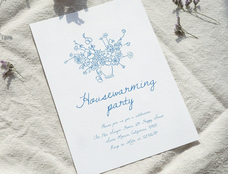 Puede incluir: Una tarjeta de invitaci&oacute;n blanca con ilustraciones florales azules y texto. La tarjeta dice "Housewarming party" en escritura cursiva, con detalles del evento e informaci&oacute;n de contacto. El dise&ntilde;o presenta un jarr&oacute;n de flores.