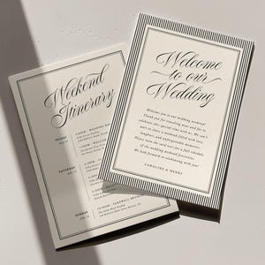 May include: Two rectangular wedding cards with black striped borders on cream paper. One card reads Welcome to our Wedding with names Caroline & Henry. The second card is titled Weekend Itinerary and lists event details for Friday, Saturday, and Sunday.