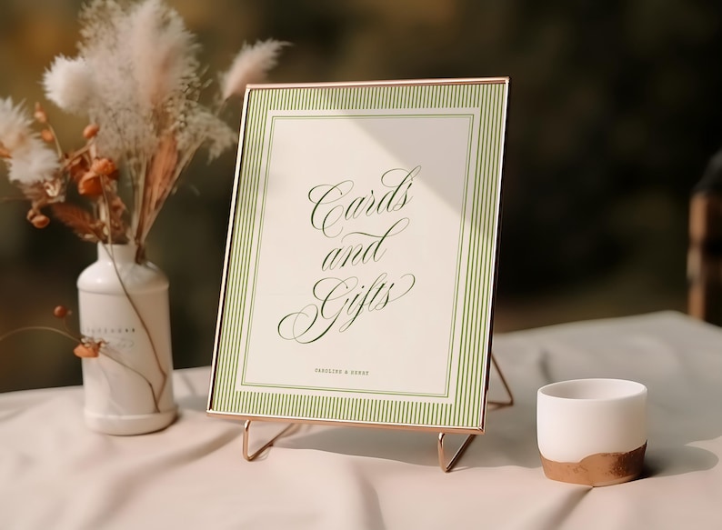 May include: A rectangular sign in a thin copper-colored frame featuring a cream-colored background with green vertical stripes and the text "Cards and Gifts" in a green cursive font, with "HANDLINE & HENRY" printed in small letters below.