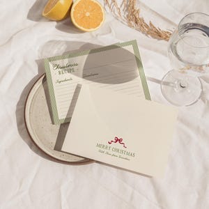 May include: A still-life image featuring a Christmas recipe card with green striped borders and a cream-colored envelope with a red bow and the words "Merry Christmas." Two lemon halves and a glass of water are also visible.