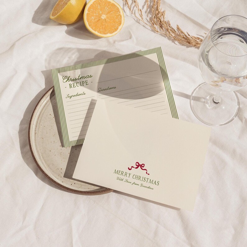 May include: A still-life image featuring a Christmas recipe card with green striped borders and a cream-colored envelope with a red bow and the words "Merry Christmas." Two lemon halves and a glass of water are also visible.