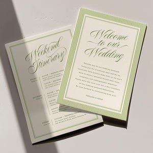 Può includere: Due cartoncini rettangolari per matrimonio con bordi a righe verdi. La carta superiore riporta la scritta Welcome to our Wedding in elegante corsivo, seguita da testo. La carta inferiore è intitolata Weekend Itinerary con un programma.