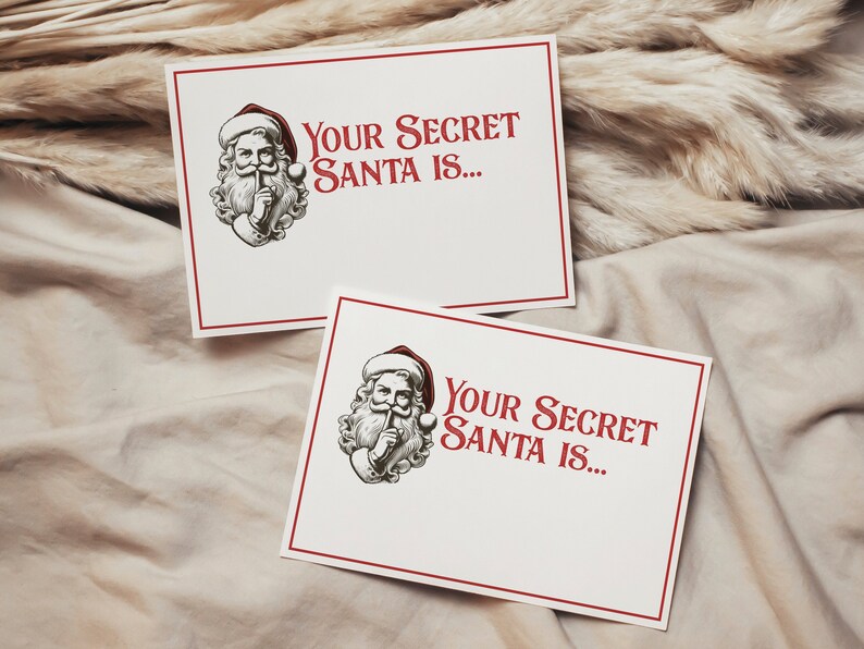May include: Two white cards with red borders and a black and white illustration of Santa Claus with his finger to his lips. The text on the cards reads "Your Secret Santa is..."