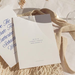May include: A white save the date card with blue calligraphy text that reads "Save the Date for Catherine & Sebastian Wedding". The date is printed in blue text below: "08 | 28 | 24 Catherine & Sebastian Mount Pleasant, SC"